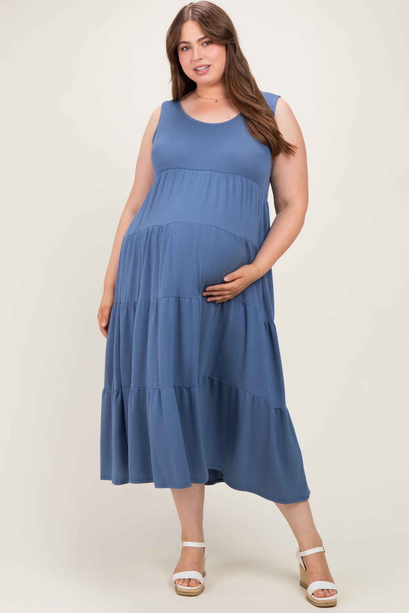 woman wearing a blue sleeveless maternity plus dress with tiered layers and holding her baby bump
