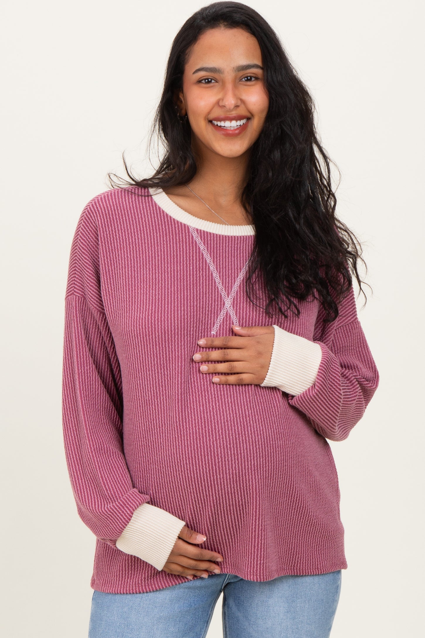 woman wearing a mauve striped maternity sweater with cream sleeves and holding her baby bump