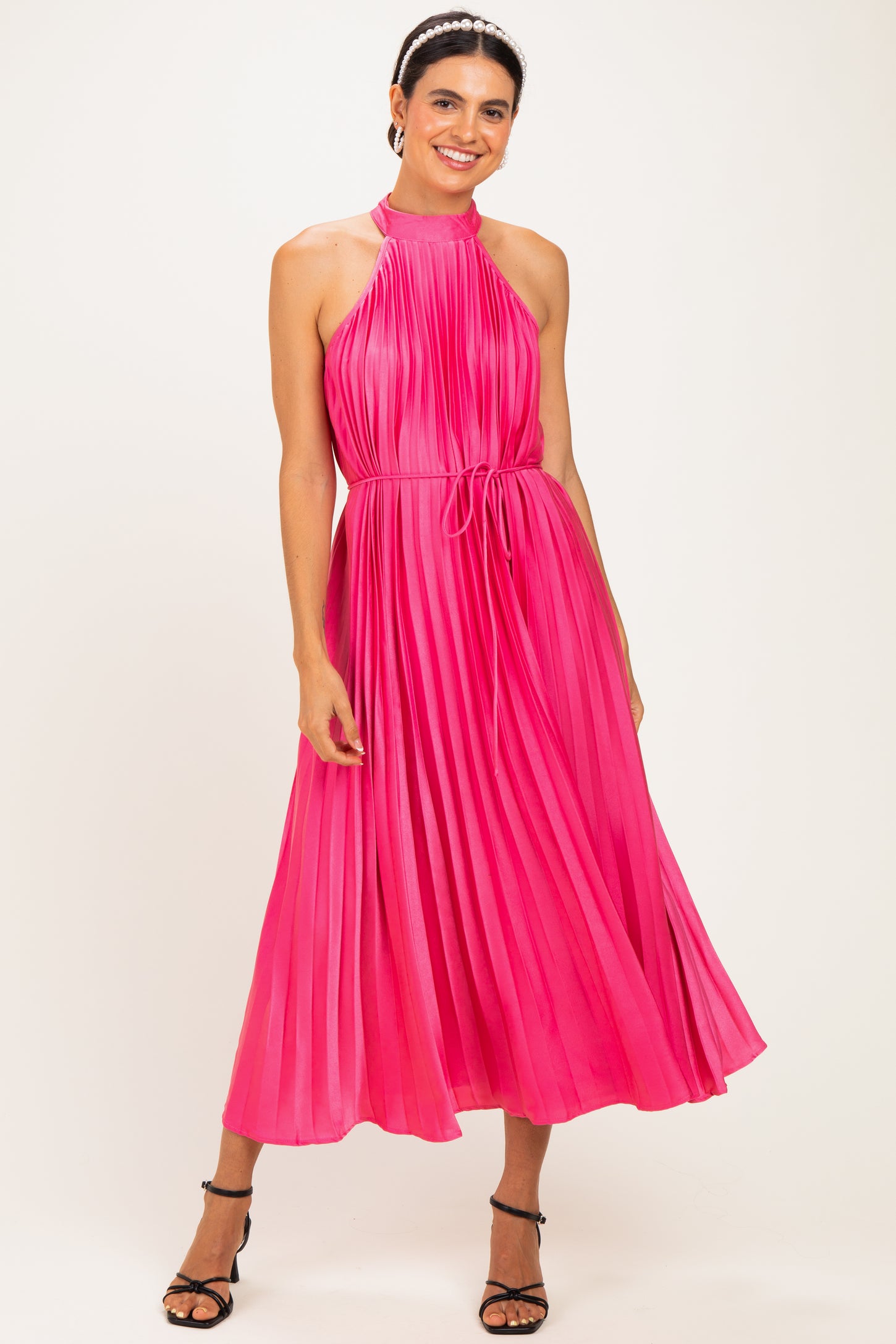 woman wearing a bright pink pleated halter neck midi dress with a tie waist and strappy black heels