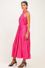 woman wearing a bright pink pleated midi dress with a halter neck and tie waist detail