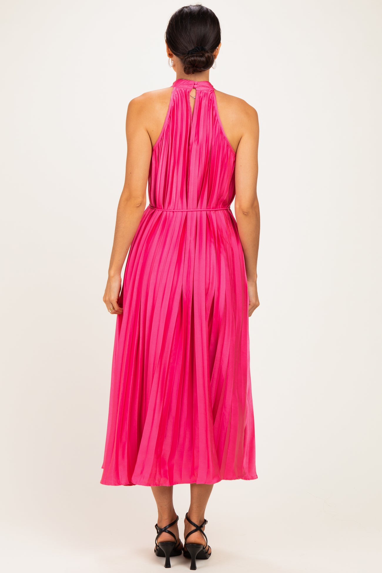 woman wearing a vibrant pink pleated midi dress with a halter neck and open back detail