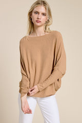 woman wearing a camel long sleeve oversized top with a boat neckline and relaxed fit paired with white pants