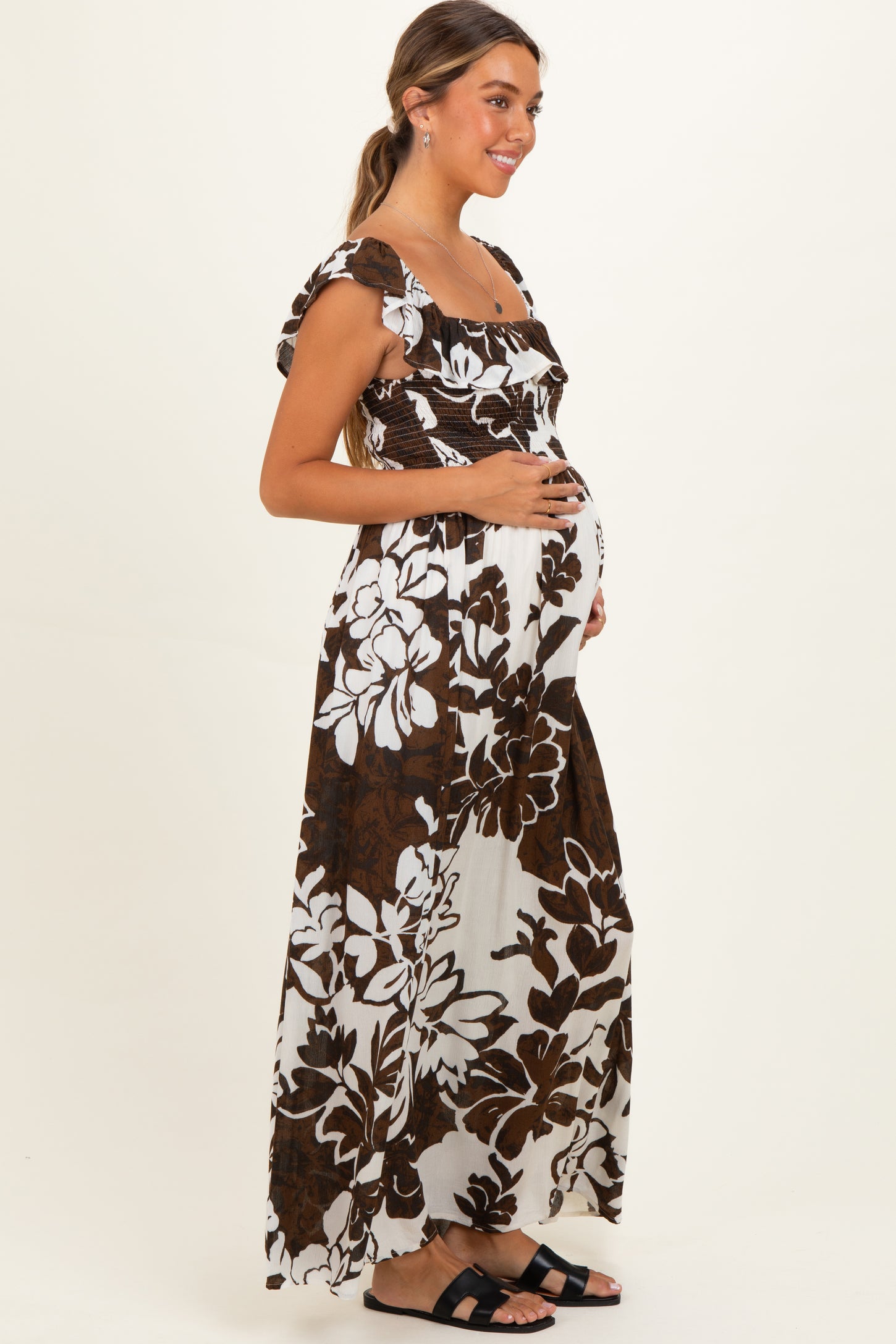 woman wearing a brown and white floral maternity maxi dress and holding her baby bump