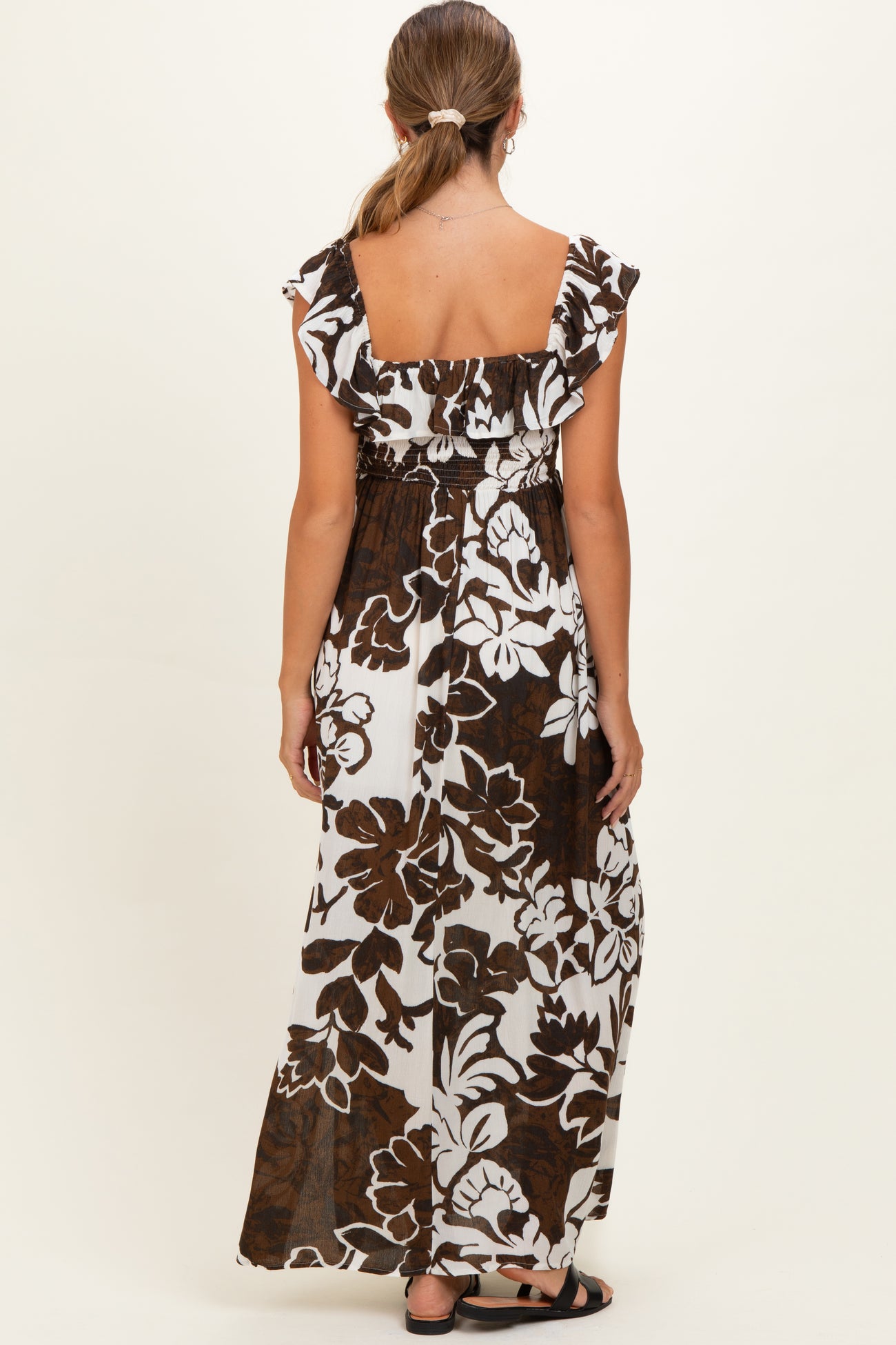 woman wearing a brown and white floral maxi maternity dress with ruffled sleeves and an elastic waist from the back