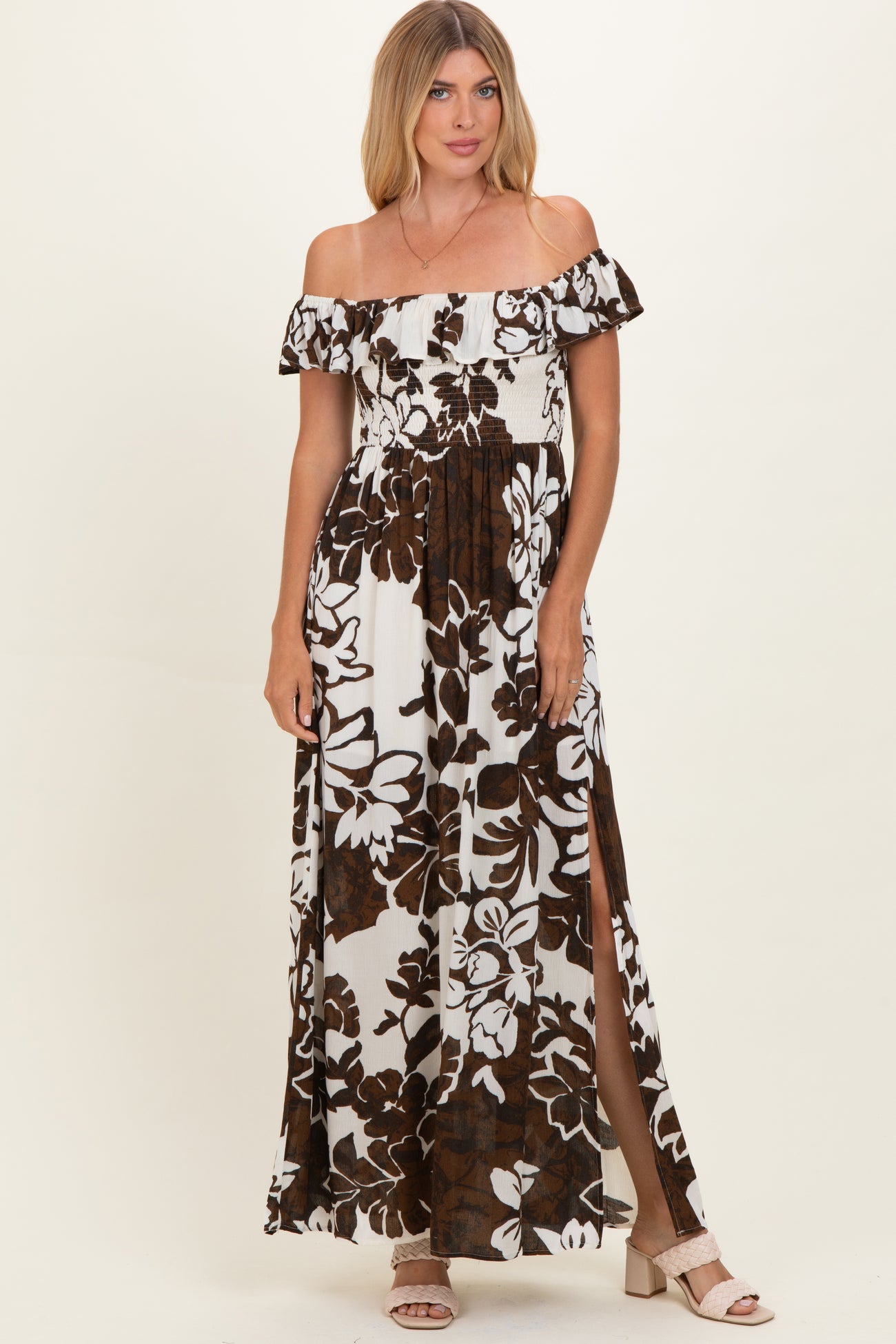 woman wearing a brown and white floral off-the-shoulder maxi dress with side slits and ruffle details