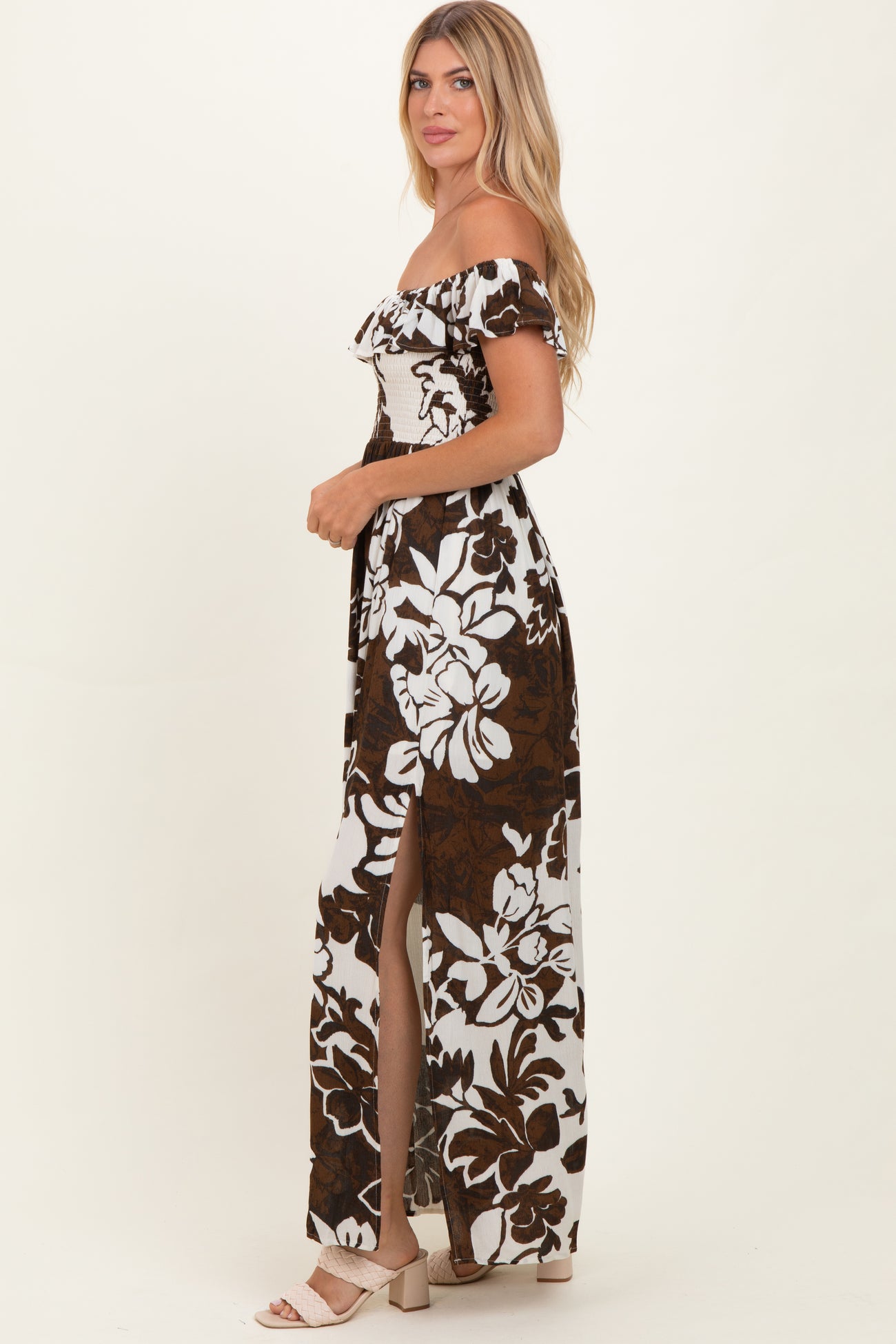 woman wearing a brown and white floral off-shoulder maxi dress with side slit and a fitted bodice