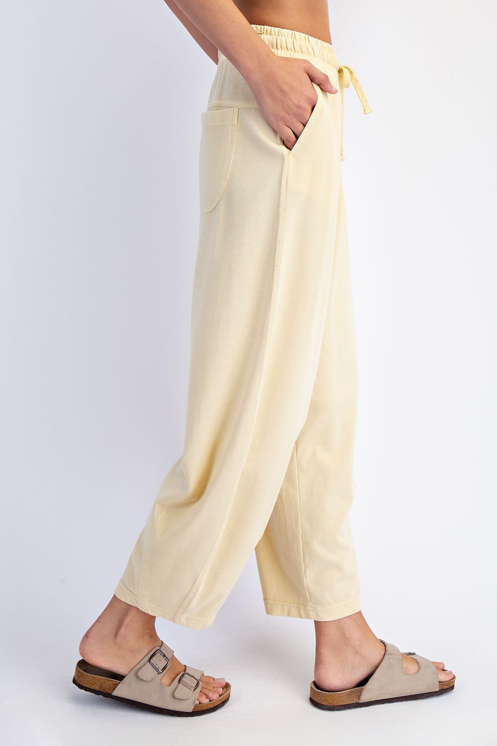 woman wearing light yellow wide-leg lounge pants with pockets and an elastic waistband, paired with tan sandals