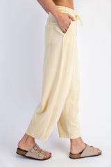 woman wearing light yellow wide-leg lounge pants with pockets and an elastic waistband, paired with tan sandals