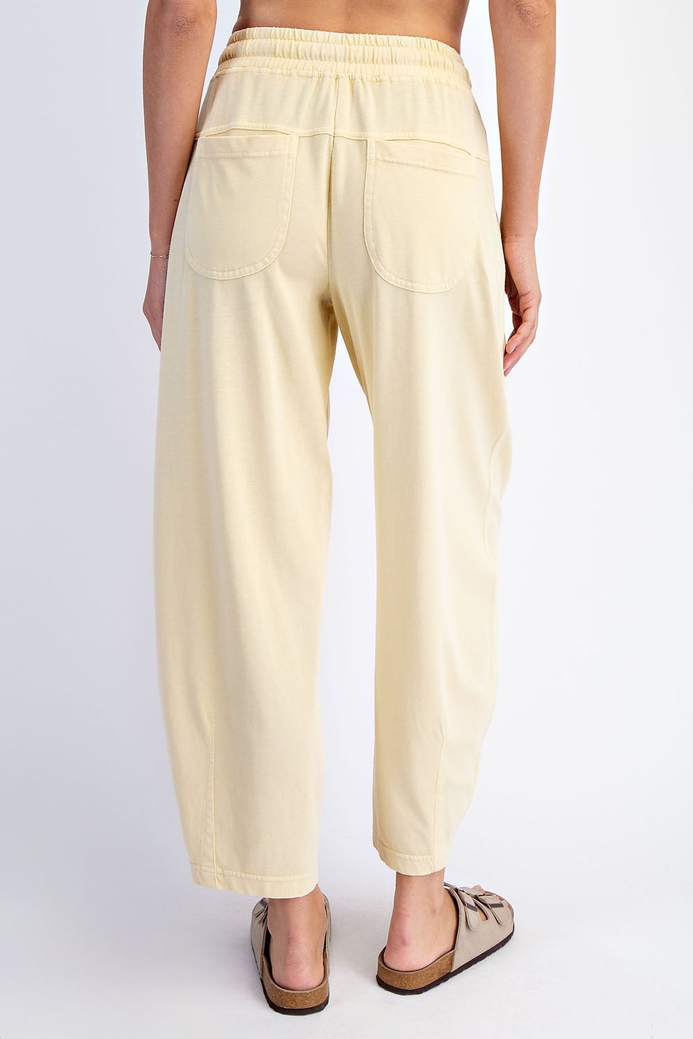 woman wearing light yellow loose-fitting pants with an elastic waistband and back pockets, viewed from the back