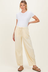 woman wearing a white short sleeve maternity top and light yellow drawstring pants, standing with one hand on her hip