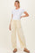 woman wearing a white short sleeve maternity top and light yellow drawstring pants, standing with one hand on her hip