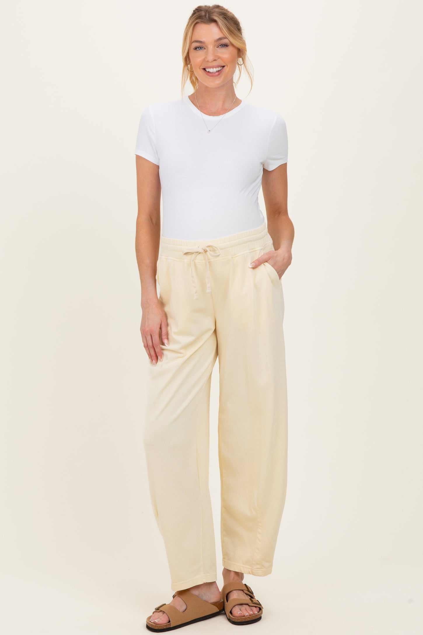 woman wearing a white short sleeve v-neck top and cream maternity pants with pockets and an elastic waistband