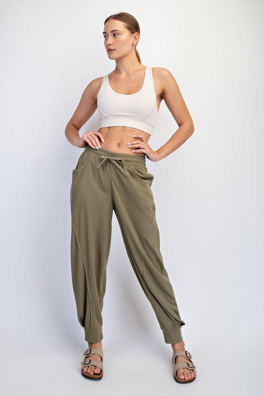 woman wearing a white sports bra and olive green relaxed fit jogger pants with side pockets