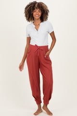 woman wearing a gray henley maternity top and rust-colored maternity joggers with pockets and elastic cuffs