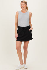 woman wearing a gray sleeveless top and a black maternity skirt with pockets, styled for comfort
