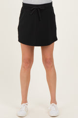 woman wearing a black maternity skort with an elastic waistband and drawstring, paired with white sneakers