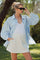 woman wearing a light blue oversized button-up shirt and gray maternity mini skirt, holding sunglasses outdoors