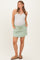 woman wearing a light green maternity skort with pockets and a white ribbed tank top, showing her baby bump
