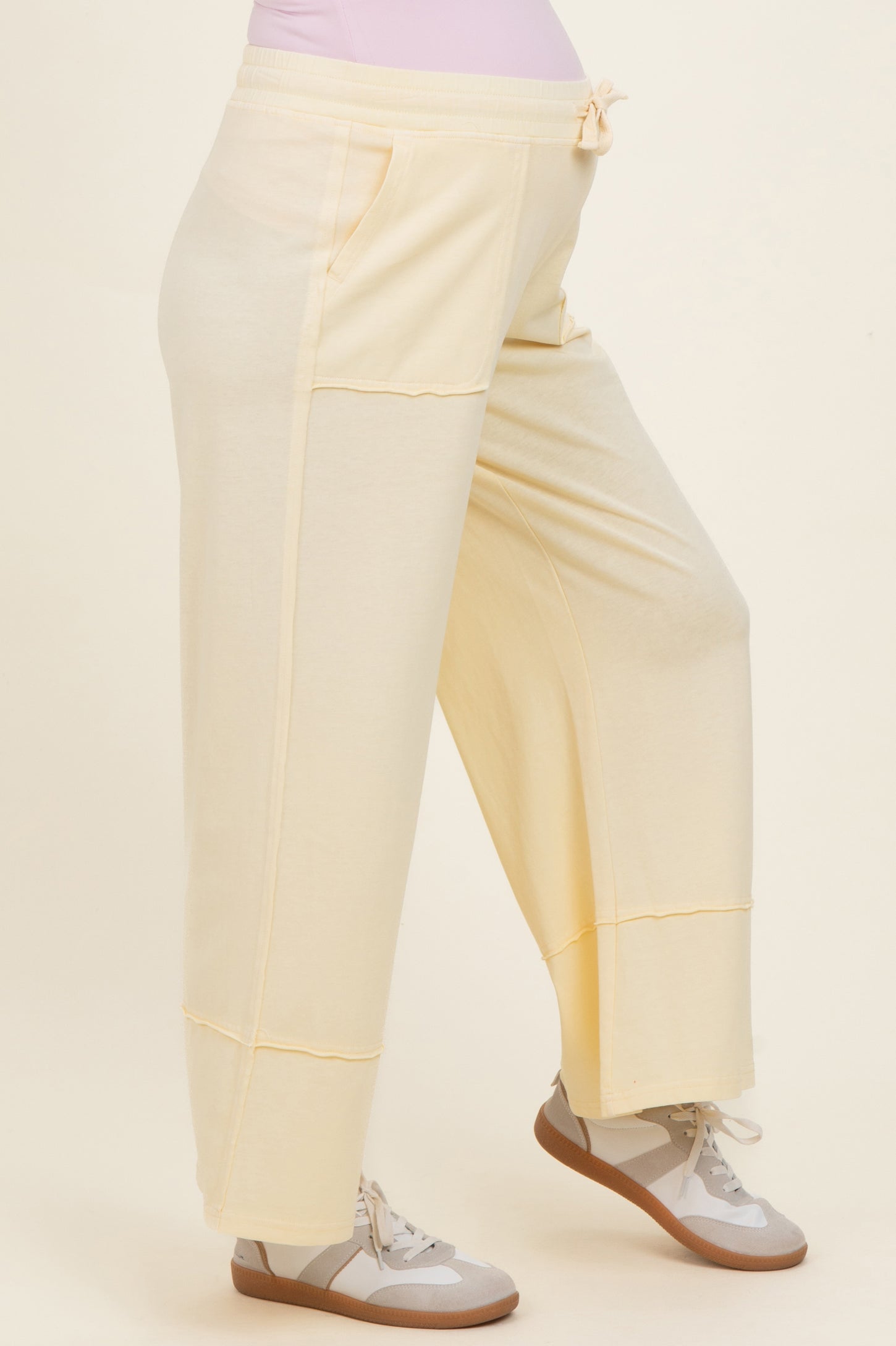 woman wearing light yellow maternity wide-leg sweatpants with pockets and a drawstring waistband, showing her baby bump