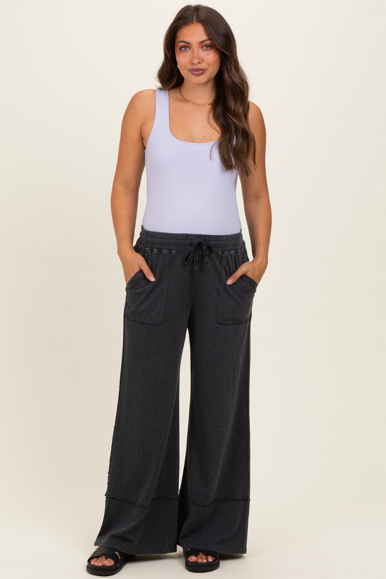woman wearing a light purple tank top and dark gray wide-leg maternity pants with pockets and drawstring waist