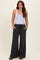 woman wearing a light purple tank top and dark gray wide-leg maternity pants with pockets and drawstring waist