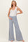 woman wearing a white tank top and light blue maternity wide leg pants, holding her baby bump