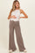 woman wearing a beige maternity tank top and wide-leg pants, holding her baby bump