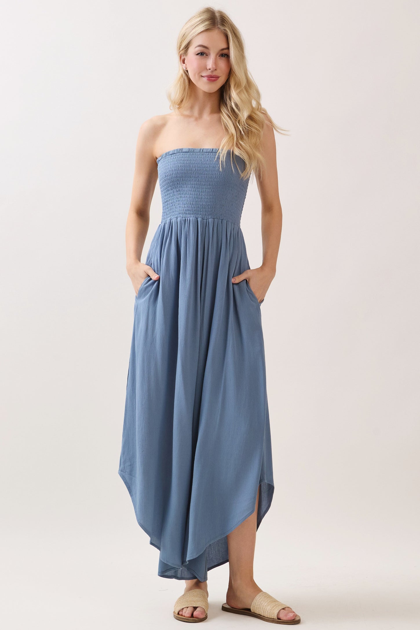 woman wearing a light blue strapless maxi dress with a smocked bodice and pockets, standing in a relaxed pose