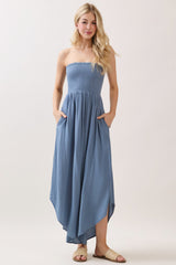 woman wearing a light blue strapless maxi dress with a smocked bodice and pockets, standing in a relaxed pose