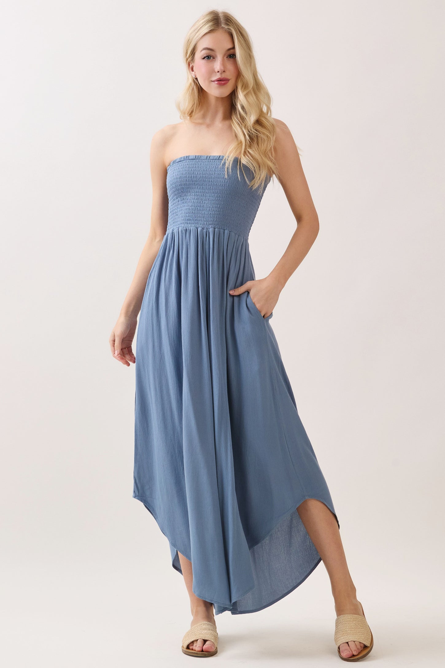 woman wearing a blue strapless maxi dress with smocked bodice and pockets, standing on a light background