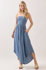 woman wearing a blue strapless maxi dress with smocked bodice and pockets, standing on a light background