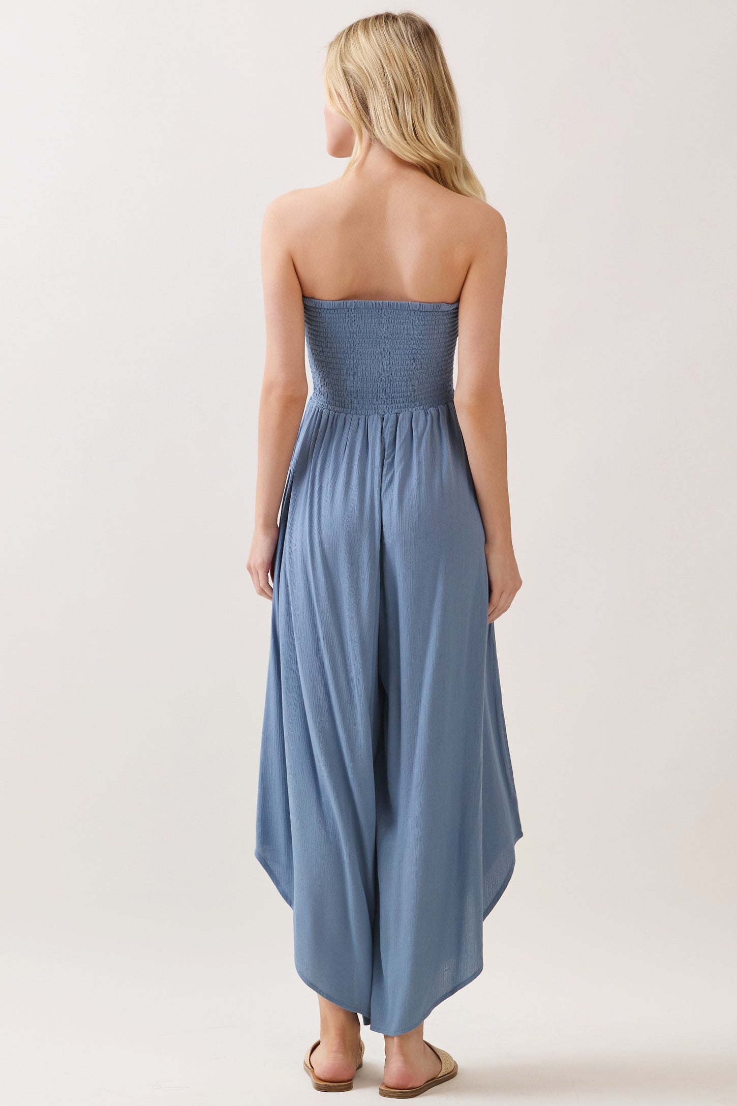 woman wearing a light blue strapless jumpsuit with a smocked bodice and flowy wide-leg pants