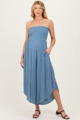 woman wearing a blue strapless maternity maxi dress with a smocked bodice and pockets, standing confidently