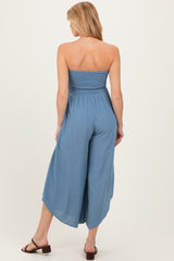 woman wearing a blue strapless maternity jumpsuit with a smocked bodice and wide leg pants, showing her back