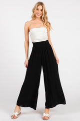 woman wearing a white crop top and black wide-leg pants, posing with one hand on her hip