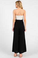 woman wearing a black wide-leg jumpsuit with a smocked waist and a satin white top, viewed from the back