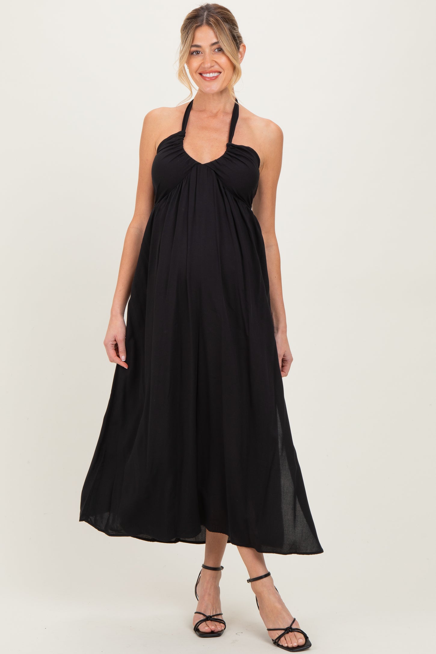 woman wearing a black halter neck maternity maxi dress with a flowing silhouette and visible baby bump