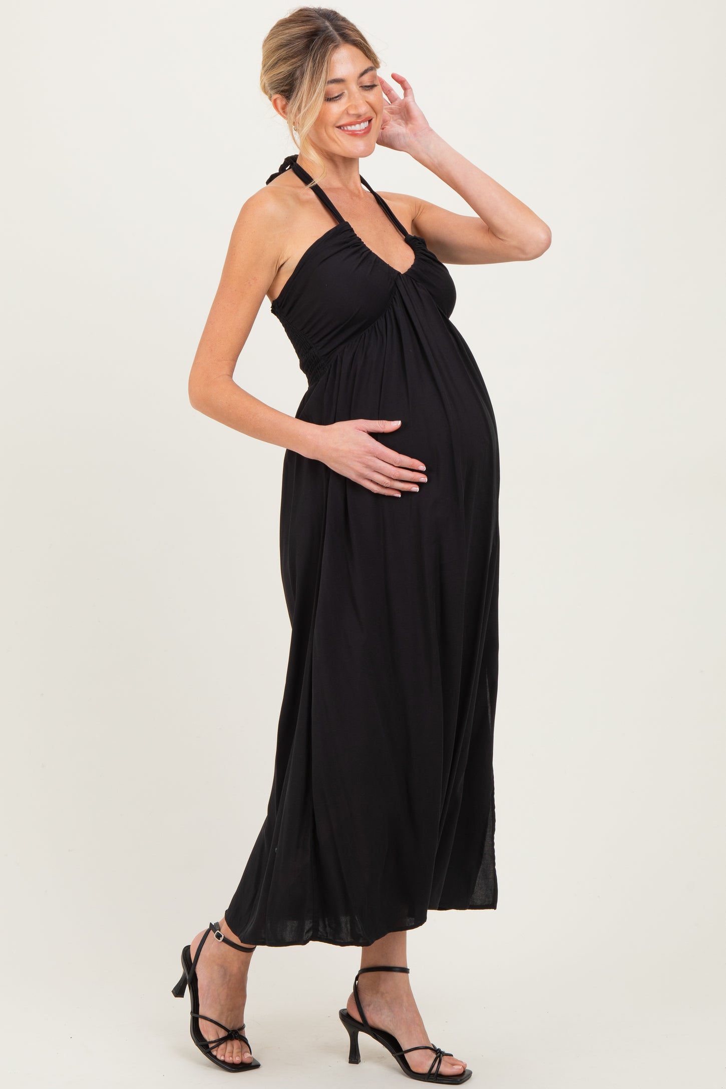 woman wearing a black halter neck maternity maxi dress and holding her baby bump