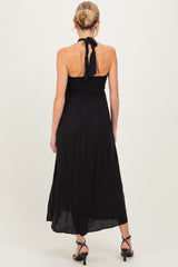 woman wearing a black maternity maxi dress with a halter neck and smocked bodice, view from the back