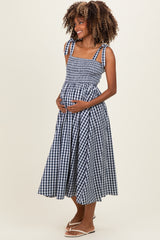 woman wearing a blue and white gingham maternity dress with a smocked bodice and holding her baby bump