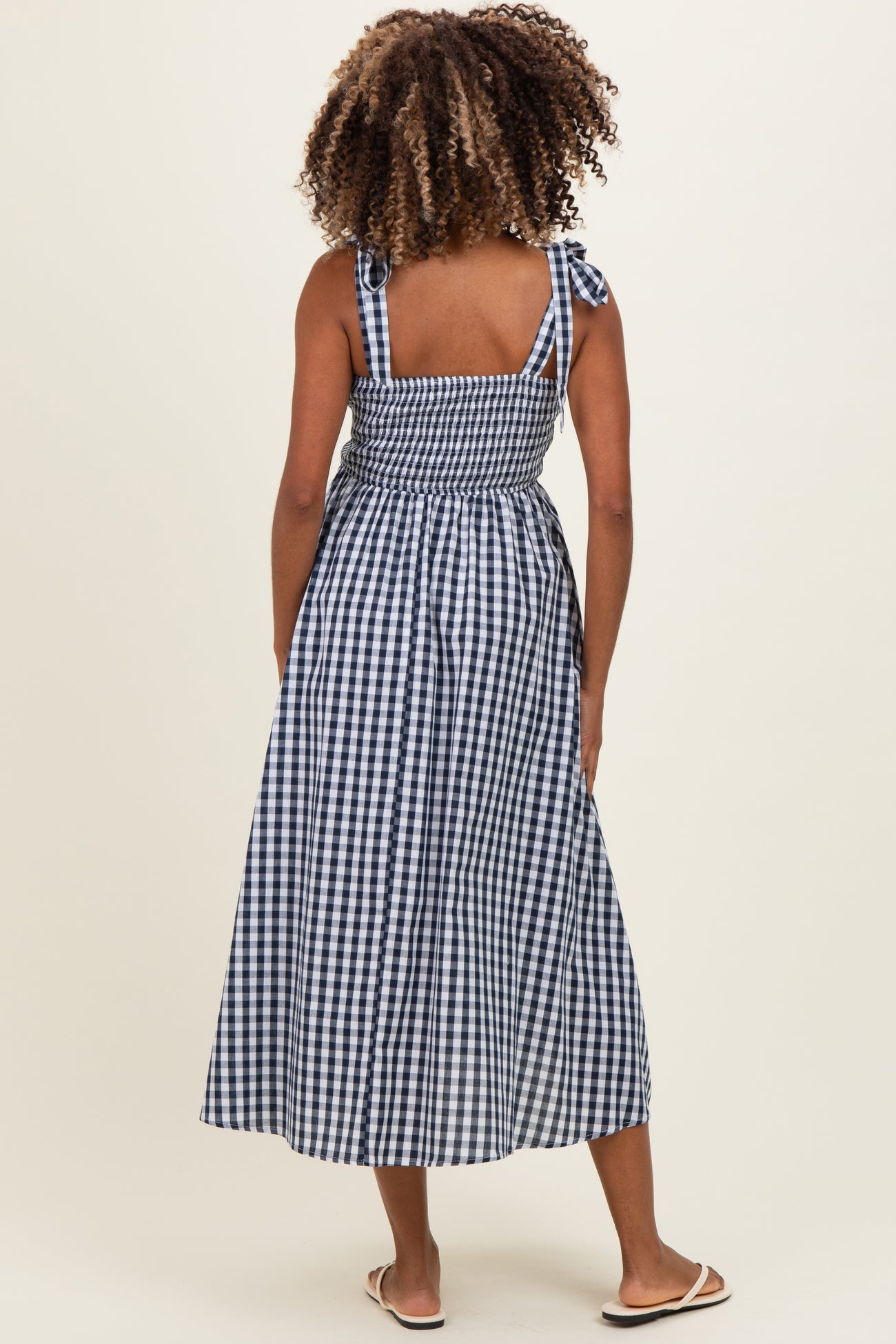 woman wearing a navy and white gingham maternity maxi dress with tie straps and a smocked back