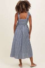 woman wearing a navy and white gingham maternity maxi dress with tie straps and a smocked back