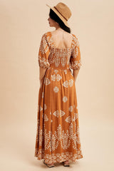woman wearing a rust-colored maxi dress with white floral patterns and puff sleeves, standing with back to camera and wearing a hat