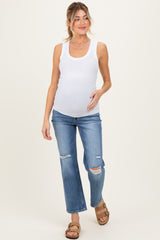 woman wearing a white ribbed tank top and distressed blue maternity jeans, gently holding her baby bump