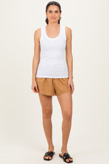 woman wearing a white tank top and brown shorts, standing with hands at her sides