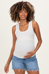 woman wearing a white ribbed maternity tank top and denim shorts, holding her baby bump