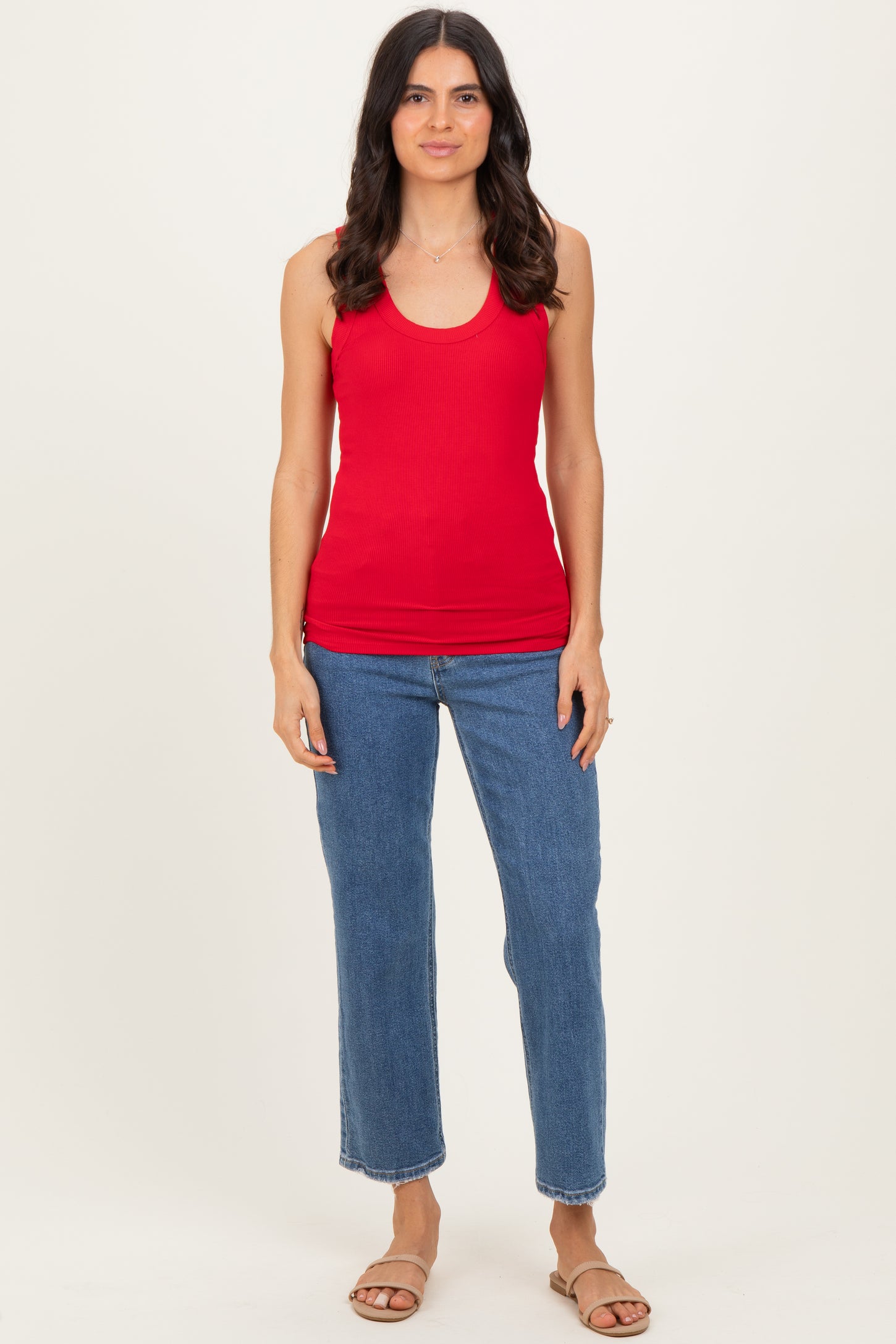 woman wearing a red ribbed tank top and blue high-waisted jeans, standing with a neutral background