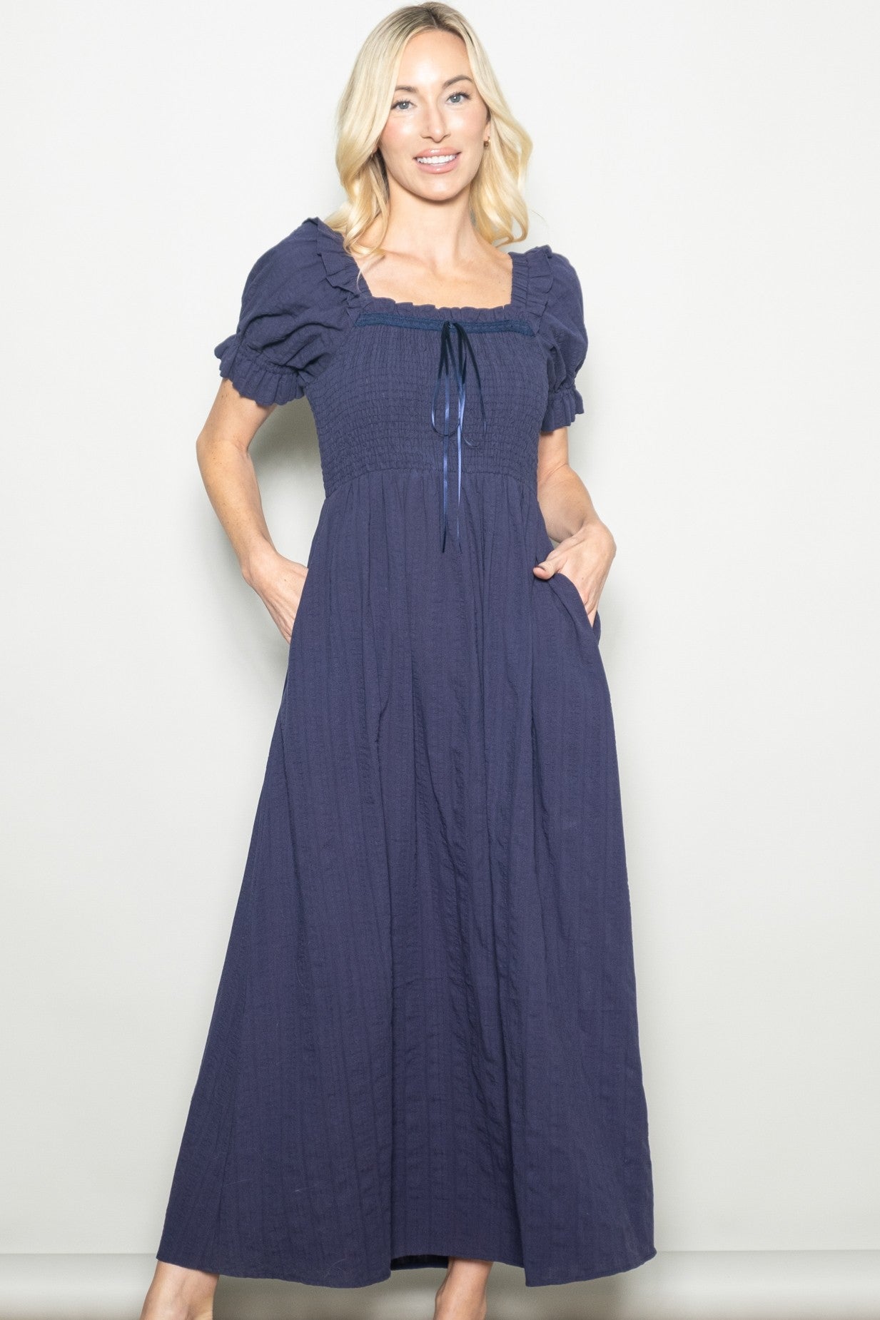 woman wearing a navy blue maxi dress with puff sleeves and a smocked bodice, featuring a drawstring and pockets