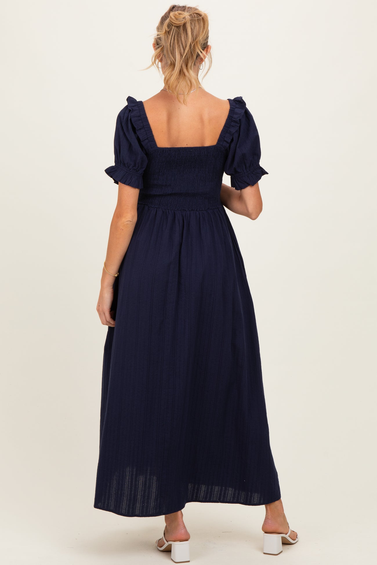 woman wearing a navy blue maternity maxi dress with short ruffled sleeves and a smocked bodice, showing a baby bump