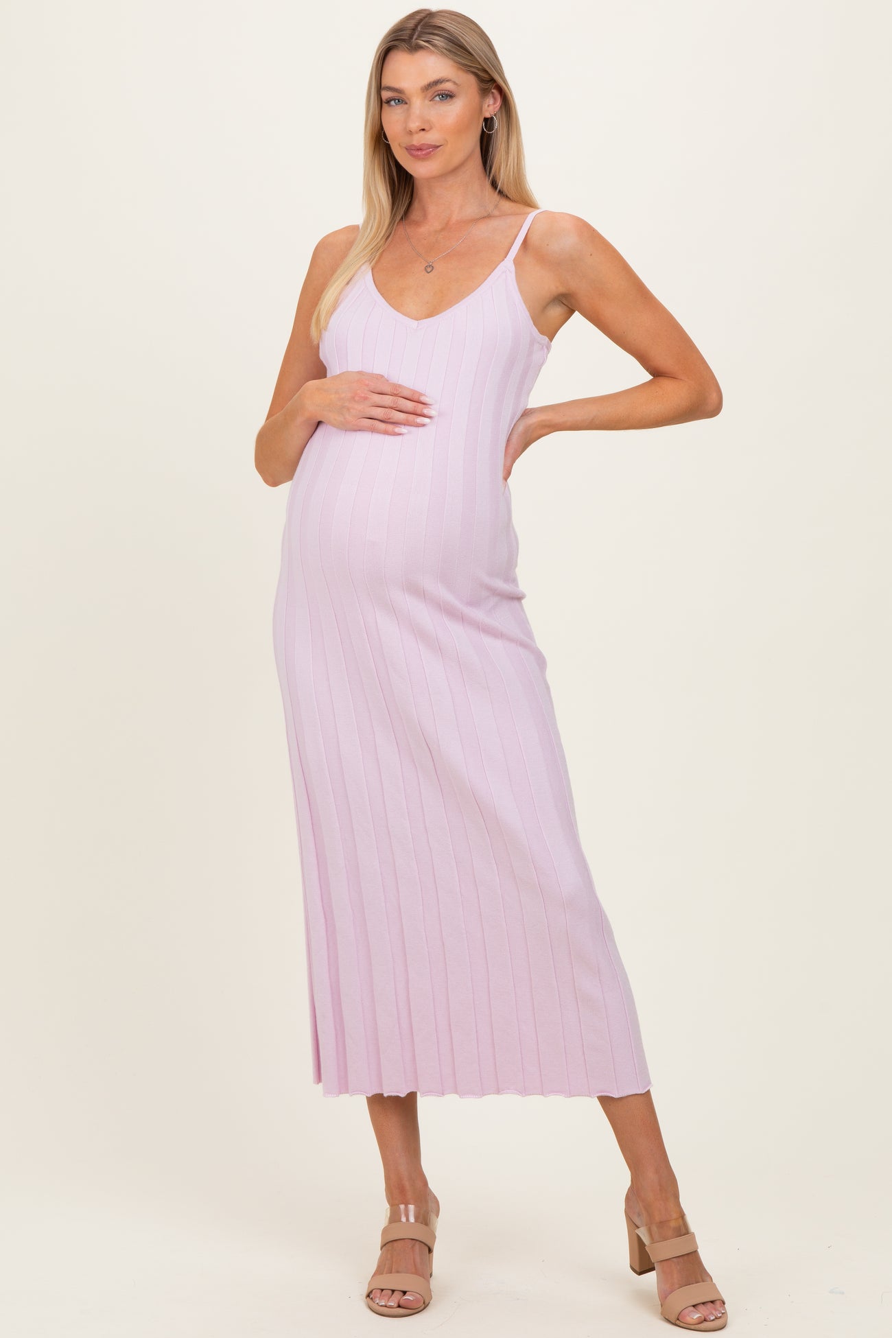 woman wearing a light pink ribbed maternity dress and holding her baby bump